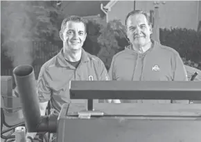  ??  ?? Instead of their usual parking spots in the lot just east of Ohio Stadium, Brian Hodges, left, and David Deiley fire up the meat smoker as they prepare to tailgate for Ohio State's football game against Nebraska at Hodges' house in Powell on Thursday. Hodges plans on 30 to 35 people in and out of his home tailgate throughout the day on Saturday.