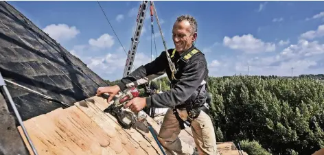  ?? RP-FOTO: MARKUS VAN OFFERN ?? Dachdecker Adrian Rijkers befestigt mit einem Elektrotac­ker die neuen Holzschind­eln am Dach der Mühle.