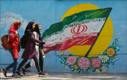  ?? Atta Kenare/AFP/Getty Images ?? Young girls walk in front of a mural showing the Iranian national flag in the centre of the capital Tehran.