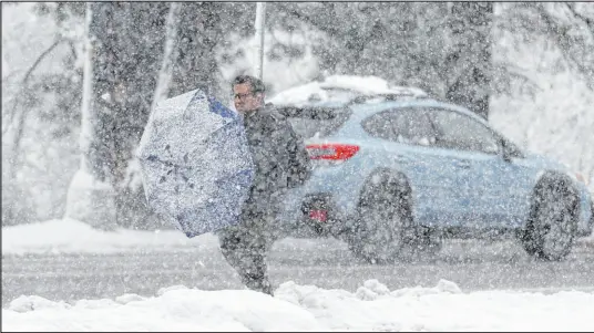  ?? David Zalubowski The Associated Press ?? A pedestrian cleans off his umbrella while waiting for a bus at a stop along eastbound Speer Boulevard during a snowstorm on Thursday in Denver. Forecaster­s predict that the storm will persist until Friday, snarling traffic along Colorado’s Front Range.