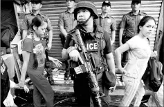  ??  ?? File photo shows a policeman holding his weapon as people pass by during a drug raid in Quezon City, Metro Manila, Philippine­s. — Reuters photo