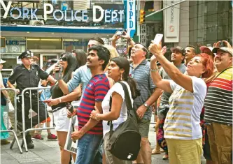  ??  ?? A New York police officer stands watch as visitors stage selfies for a giant monitor playback in Times Square on Friday in New York.