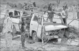  ?? AP/PTI ?? A Somali soldier, left, stands by the wreckage of a passing minibus that was destroyed in a suicide car bomb attack near the defense ministry compound in Mogadishu.