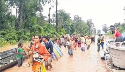  ?? PHOTO: REUTERS ?? Survivors . . . People walk through a flooded area after being brought to safety by boat in Sanam Xay district, Attapeu province, after a hydro dam under constructi­on in Southern Laos collapsed.