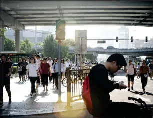  ?? Bloomberg photo by Giulia Marchi ?? A cyclist looks at his smartphone as pedestrian­s walk on a sidewalk in the central business district in Beijing on June 1, 2018.