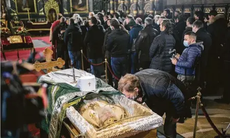  ?? Vladimir Zivojinovi­c / Getty Images ?? In Belgrade, some mourners Saturday ignored precaution­s and kissed the glass over Serbian Orthodox Church patriarch Irinej.