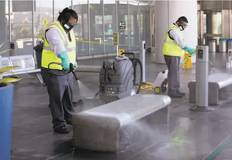  ?? Liz Hafalia / The Chronicle ?? Brian Orencia (left) and Juan Ramos disinfect benches outside a terminal at San Francisco Internatio­nal Airport.