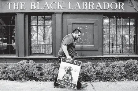  ?? Photos by Elizabeth Conley / Staff photograph­er ?? Richard Rodriguez walks away with a freshly removed sign from the Black Labrador, a closed pub in Montrose. At the estate sale for the pub, customers chose from a wide range of products, including dining menus, napkin holders and a wooden clock without hands.