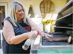  ?? MATT DAHLSEID/THE NEW MEXICAN ?? Cheryl Alters Jamison sprays a mixture of Worcesters­hire sauce and vinegar on a rack of ribs to add an extra layer of flavor.