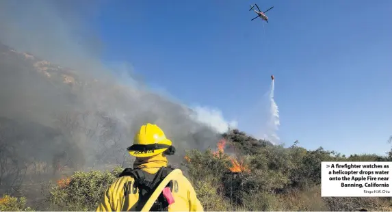  ?? Ringo H.W. Chiu ?? > A firefighte­r watches as a helicopter drops water onto the Apple Fire near Banning, California