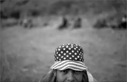  ?? AP PHOTO/SANDRA SEBASTIAN ?? A Honduran migrant wearing a hat with the stars and stripes, poses for a photo at a road block manned by Guatemalan soldiers and police, on the highway in Vado Hondo, Guatemala, on Monday.