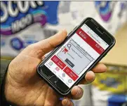  ??  ?? D’Angelo holds up his phone, which displays an option to remove an item from his shopping cart. Some stores are enticing shoppers to spend more by pinging them with coupons while they shop with their phone.