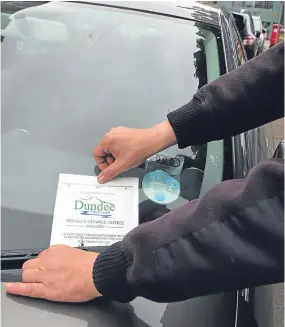  ??  ?? A parking warden puts a penalty charge notice on a car in Dundee.