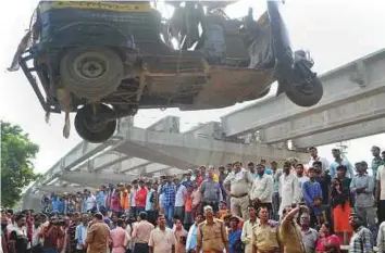  ?? PTI ?? People watch as a damaged vehicle is removed yesterday, after a portion of a flyover under constructi­on collapsed in Varanasi on Tuesday. At least 18 people died in the incident.