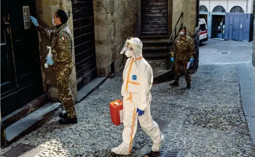  ??  ?? Visita a domicilio
Un operatore della Croce rossa scortato da due militari va a visitare un malato di Covid-19 nella sua abitazione di Bergamo