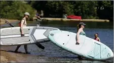  ?? PAUL CONNORS — BOSTON HERALD ?? Jako Hildebrand­t, left, and his wife Jessica Hildebrand­t, right, carry their paddle boards into the water of Lake Massapoag on Saturday in Sharon.