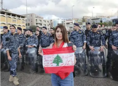  ?? AFP ?? A Lebanese anti-government protester holds a national flag in front of members of the internal security forces as she takes part in a rally in Baabda near Beirut.
