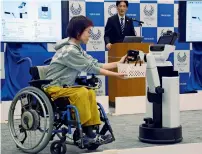  ?? AP ?? A robot passes a basket containing drinks to a woman in wheelchair during the unveiling event in Tokyo on Friday. —