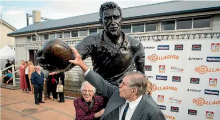  ??  ?? Sir Colin Meads touches the rugby ball his statue holds after its unveiling, as Dame Verna looks on at Te Kuiti.