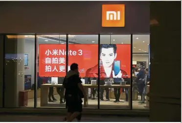  ?? — Reuters ?? Listing exercise: People walk past a Xiaomi store in Beijing. The smartphone maker and existing investors are offering 2.18 billion shares at HK$17 to HK$22 apiece under its IPO.