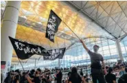  ?? AP PHOTO/KIN CHEUNG ?? Protesters wave flags at the Hong Kong Internatio­nal Airport on Monday. One of the world’s busiest airports canceled all flights after thousands of pro-democracy protesters crowded into the main terminal.