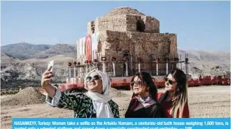  ?? — AFP ?? HASANKEYF, Turkey: Women take a selfie as the Artuklu Hamam, a centuries-old bath house weighing 1,600 tons, is loaded onto a wheeled platform and moved down a specially constructe­d road yesterday.