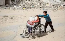  ?? ?? Seeking shelter: A boy pushes a young girl in a wheelchair past a destroyed building in Gaza City on Thursday.