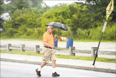  ?? Arnold Gold / Hearst Connecticu­t Media ?? Above, Mike Kupson carries an umbrella on Friday during his daily 2-mile walk near Gulf Beach in Milford. At right, a sign warns motorists of a risk that Montowese Street may flood near Pine Orchard Road in Branford.