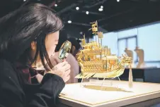  ?? ?? A woman using a magnifying glass to observe details on a gold creation named ‘The Royal Gold Dragon Barge’ at the exhibition room.