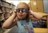  ?? AP FILE PHOTOS ?? Emmalyn Johnson, 3, tries on a pair of eclipse glasses at Mauney Memorial Library in Kings Mountain, N.C., on Aug. 2. Experts warn not to try to view the eclipse without wearing glasses specially designed to withstand the intensity of the sun’s rays.
