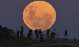  ??  ?? People watch as the ‘super flower blood moon’ rises over Bondi Beach in Sydney on 26 May, 2021. Guardian Australia’s picture editor explains how to photograph the moon whether you’re using a phone or DSLR camera, and the best settings to use. Photograph: Anadolu Agency/Getty Images