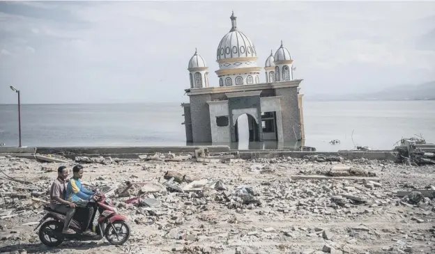  ?? PICTURE: CARL COURT/GETTY IMAGES ?? 0 The remains of a mosque that was moved by the earthquake stands forlornly in the water in Palu, Indonesia, as survivors pass by