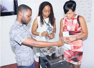  ??  ?? Keenan Clarke (left), final-year student at the Edna Manley College of the Visual and Performing Arts, explains how he incorporat­ed Jamaican proverbs into his jewellery to Gillian Hyde (right), general manager, JN Small Business Loans, and Miriam...