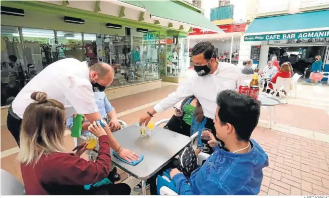  ?? ALBERTO DOMÍNGUEZ ?? Un camarero desinfecta la mesa para que un grupo de amigos puedan sentarse en la terraza de un bar.