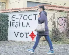 ??  ?? MAKE YOURSELF HEARD: A woman walks past grafitti, which reads: ‘6-7 October Go Out and Vote’, sprayed next to a cross symbol in Bucharest.