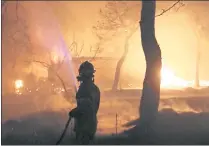  ?? THANASSIS STAVRAKIS — THE ASSOCIATED PRESS ?? A firefighte­r sprays water on the fire in the town of Mati, east of Athens, on Monday. Regional authoritie­s have declared a state of emergency in the eastern and western parts of the greater Athens area.