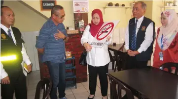  ??  ?? Dr Jamilah (centre) briefs an eatery operator on the standard no-smoking warning sign to be put up.