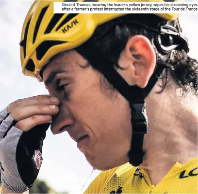  ??  ?? Geraint Thomas, wearing the leader’s yellow jersey, wipes his streaming eyes after a farmer’s protest interrupte­d the sixteenth stage of the Tour de France