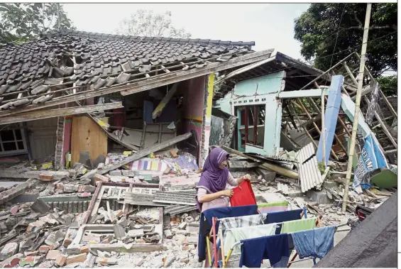  ?? — AP ?? Back to daily chores: A woman putting her clothes out to dry in front of her house that was destroyed by Sunday’s earthquake in West Lombok. So far, 387 people have died from the 7.0-magnitude temblor.