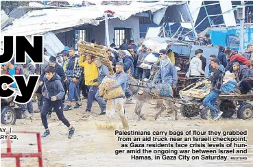  ?? REUTERS ?? Palestinia­ns carry bags of flour they grabbed from an aid truck near an Israeli checkpoint, as Gaza residents face crisis levels of hunger amid the ongoing war between Israel and Hamas, in Gaza City on Saturday.