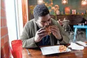  ?? ERIN WOODIEL/SIOUX FALLS ARGUS LEADER ?? Langston Newton eats his final burger to try all 32 from the Downtown Burger Battle on Jan. 21 at Swamp Daddy’s in Sioux Falls.