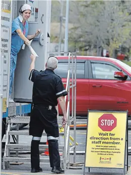  ?? CLIFFORD SKARSTEDT EXAMINER ?? A health-care worker hands documents to a city paramedic at the COVID-19 assessment centre at PRHC on Saturday . Ontario had 427 new cases Tuesday, bringing the total to date to 23,384 across the province.