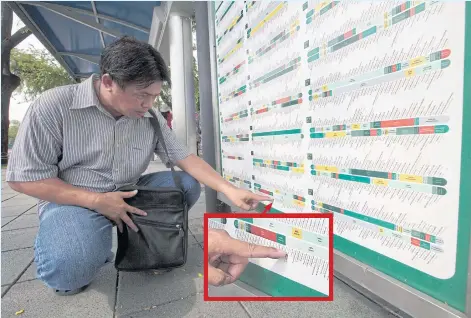  ??  ?? A bus passenger squats down to read a city bus route at a bus stop in the Sanam Luang area of the city.