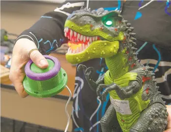  ??  ?? A button that was created using a 3-D printer activates a toy Tyrannosau­rus rex making it much easier to use for a child with a disability or diminished motor skills.