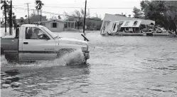  ??  ?? A truck drives through floodwater­s Saturday past a home damaged by Hurricane Harvey in Aransas Pass, Texas. Harvey rolled over the Texas Gulf Coast, smashing homes and businesses and lashing the shore with wind and rain so intense that drivers were...