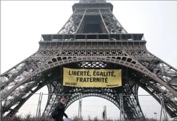  ??  ?? A woman passes by as activists unfurl a banner on the Eiffel Tower which reads “Liberty, Equality, Fraternity” .