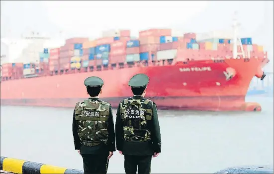  ?? -/AFP ?? Dos policías chinos observan la llegada de un carguero portaconte­nedores al puerto de Qingdao