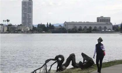  ??  ?? A woman wears a face mask while walking at Lake Merritt. Nooses were found hanging in trees inthe area. Photograph: Jeff Chiu/AP