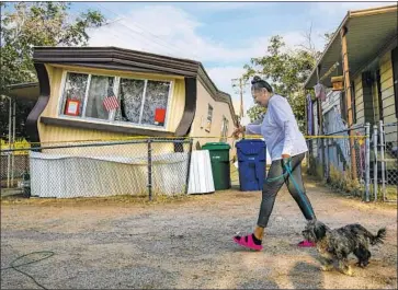  ?? Irfan Khan Los Angeles Times ?? CARMEN RIVERA walks her dog, Ash, past a Trousdale Estates mobile home in Ridgecrest that was dislodged in the 6.4 magnitude earthquake. Early Friday, a magnitude 5.4 aftershock struck near the epicenter.