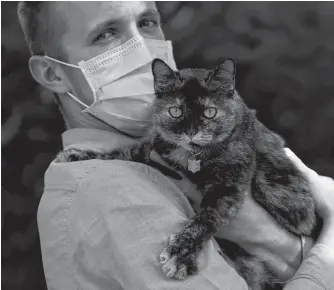  ?? CHRISTIAN HARTMANN/REUTERS ?? Brian, 24 year-old, suspected to have been infected by the SARS-COV-2 poses in his garden with Papille, his 9 year-old cat who recovered after being tested positive for the virus amid the coronaviru­s disease (COVID-19) outbreak, in Athis-mons, near Paris, France on Wednesday.